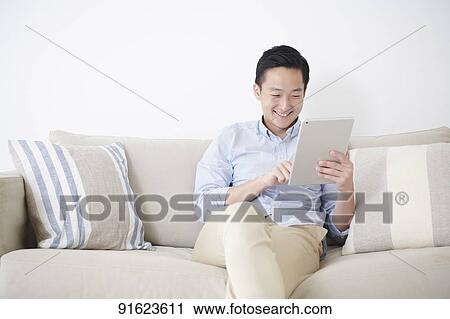 Young Japanese man using tablet on the sofa View Large Photo Image Stock Image - Young Japanese man using tablet on the sofa. Fotosearch