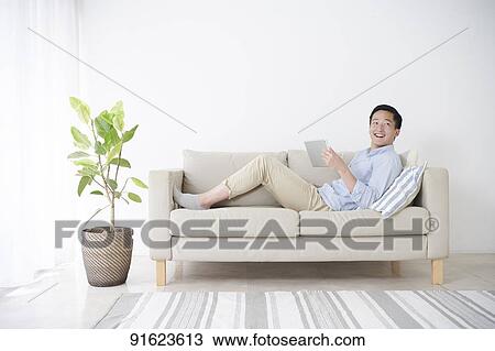Young Japanese man using tablet on the sofa View Large Photo Image Stock Image - Young Japanese man using tablet on the sofa. Fotosearch