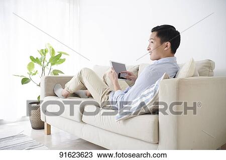 Young Japanese man using tablet on the sofa View Large Photo Image Stock Image - Young Japanese man using tablet on the sofa. Fotosearch