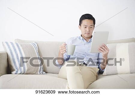 Young Japanese man using tablet on the sofa View Large Photo Image Stock Photo - Young Japanese man using tablet on the sofa. Fotosearch