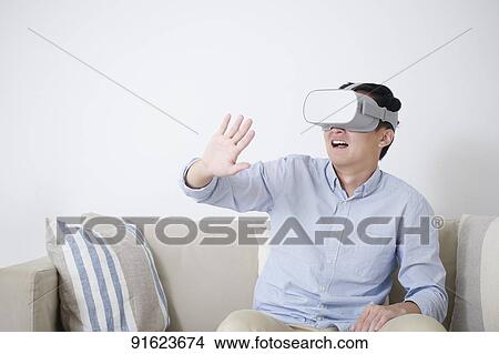 Picture - Young Japanese man using VR goggles. Fotosearch