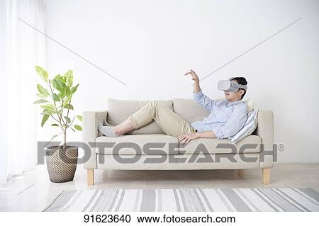 Stock Image - Young Japanese man using VR goggles. Fotosearch
