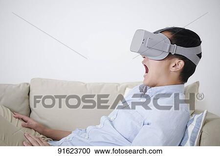 Stock Image - Young Japanese man using VR goggles. Fotosearch
