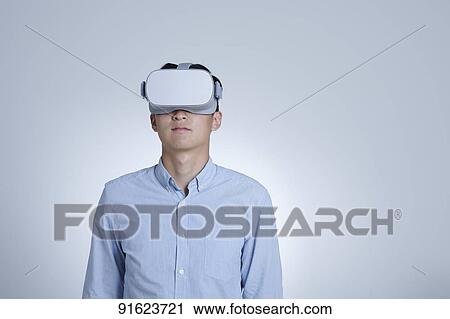 Stock Image - Young Japanese man using VR goggles. Fotosearch