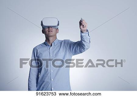 Stock Image - Young Japanese man using VR goggles. Fotosearch