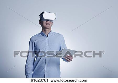 Stock Image - Young Japanese man using VR goggles. Fotosearch