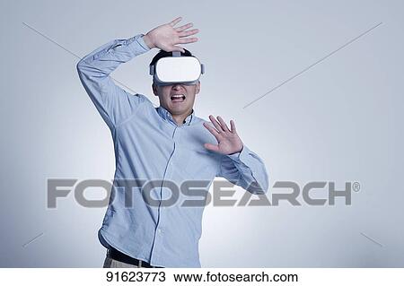 Stock Image - Young Japanese man using VR goggles. Fotosearch