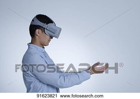 Stock Image - Young Japanese man using VR goggles. Fotosearch