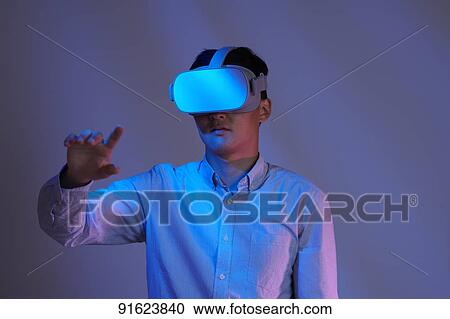 Stock Image - Young Japanese man using VR goggles. Fotosearch