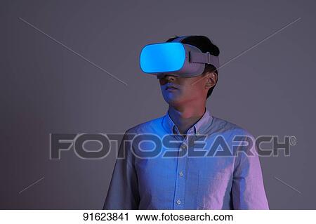 Stock Image - Young Japanese man using VR goggles. Fotosearch