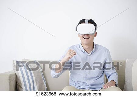 Stock Photo - Young Japanese man using VR goggles. Fotosearch