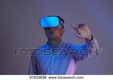 Stock Photo - Young Japanese man using VR goggles. Fotosearch