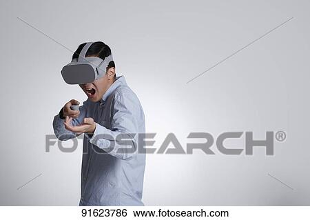 Stock Photograph - Young Japanese man using VR goggles. Fotosearch