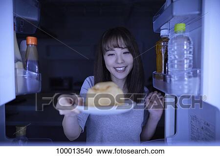 Stock Image - Young Japanese woman eating night snack from the fridge. Fotosearch