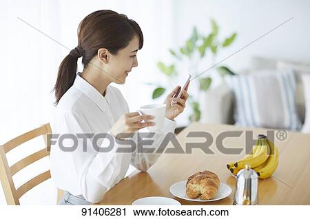 Stock Image - Young Japanese woman having breakfast at home. Fotosearch