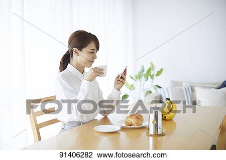 Stock Image - Young Japanese woman having breakfast at home. Fotosearch