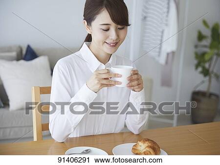 Stock Image - Young Japanese woman having breakfast at home. Fotosearch