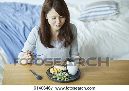 Stock Photo - Young Japanese woman having breakfast at home. Fotosearch