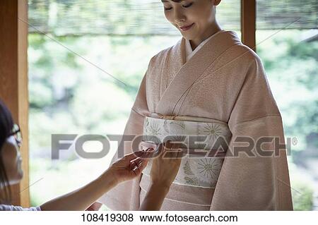 Stock Photo - Young Japanese woman putting on traditional kimono. Fotosearch