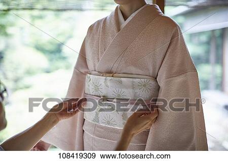 Stock Photo - Young Japanese woman putting on traditional kimono. Fotosearch