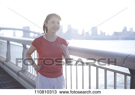 Stock Image - Young Japanese woman running downtown Tokyo. Fotosearch