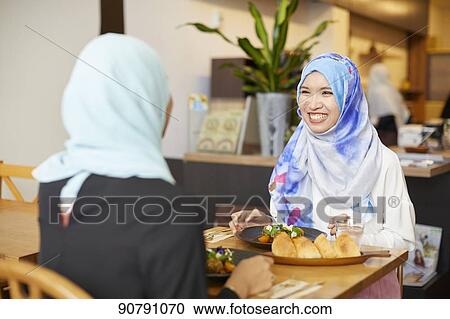 Stock Image - Young South-east Asian women eating at restaurant. Fotosearch
