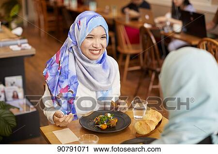Stock Image - Young South-east Asian women eating at restaurant. Fotosearch