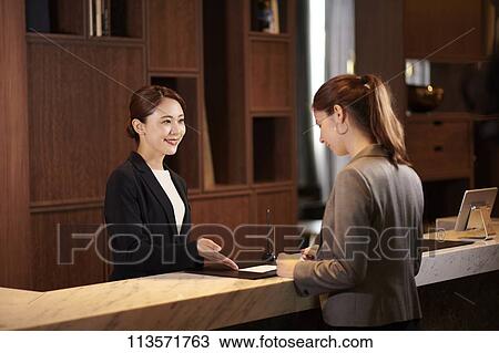 Stock Image - Young woman checking in at a hotel. Fotosearch