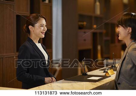 Stock Image - Young woman checking in at hotel. Fotosearch
