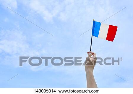 Picture - Hand holding flag against blue sky. Fotosearch