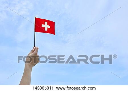 Stock Image - Hand holding flag against blue sky. Fotosearch