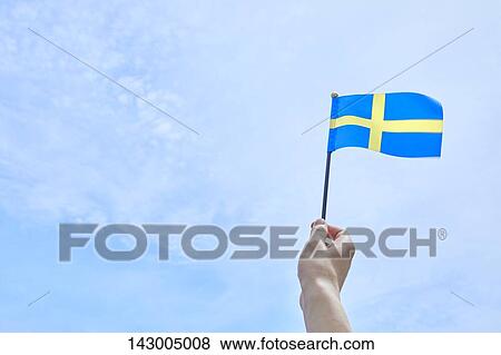 Hand holding flag against blue sky View Large Photo Image Stock Photo - Hand holding flag against blue sky. Fotosearch