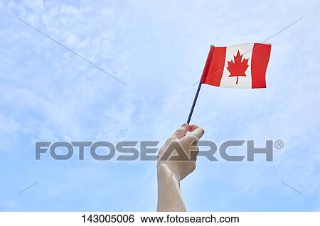 Stock Photograph - Hand holding flag against blue sky. Fotosearch