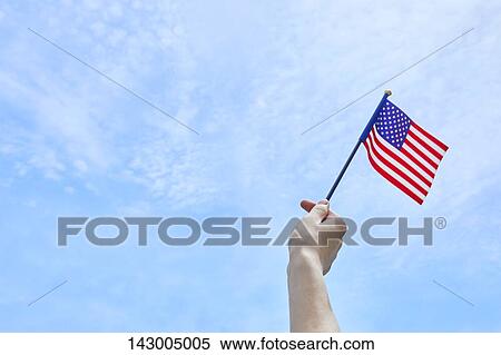 Hand holding flag against blue sky View Large Photo Image Stock Photography - Hand holding flag against blue sky. Fotosearch