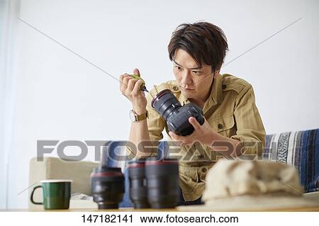 Stock Image - Japanese man cleaning camera at home. Fotosearch