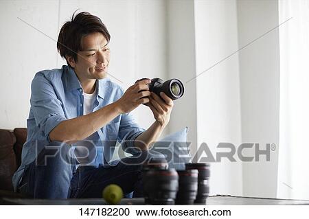 Stock Image - Japanese man cleaning camera at home. Fotosearch