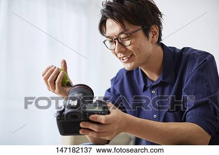 Stock Photo - Japanese man cleaning camera at home. Fotosearch