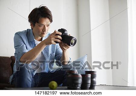 Stock Photo - Japanese man cleaning camera at home. Fotosearch