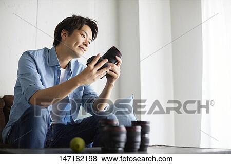 Stock Photo - Japanese man cleaning camera at home. Fotosearch