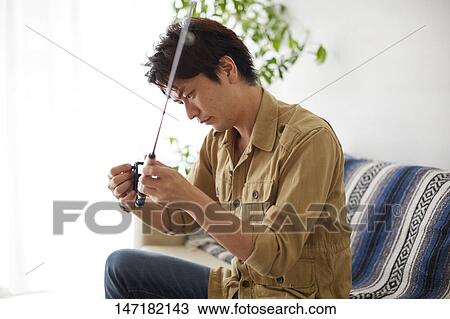 Stock Image - Japanese man cleaning fishing rod at home. Fotosearch