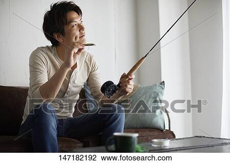 Stock Image - Japanese man cleaning fishing rod at home. Fotosearch