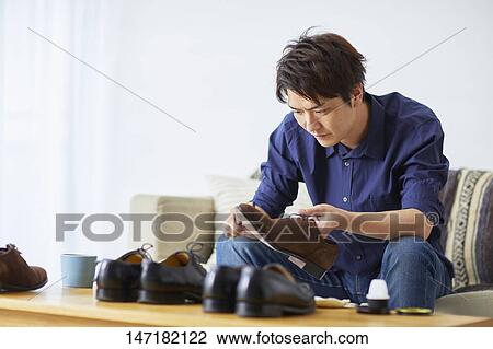 Stock Image - Japanese man cleaning shoes at home. Fotosearch
