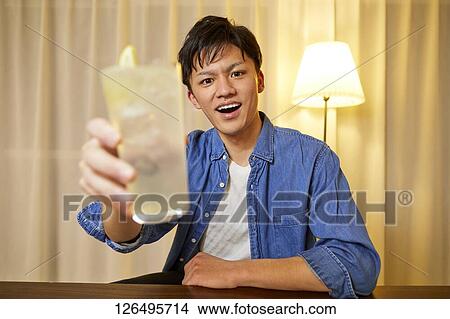 Picture - Japanese man drinking at home remote drinking. Fotosearch