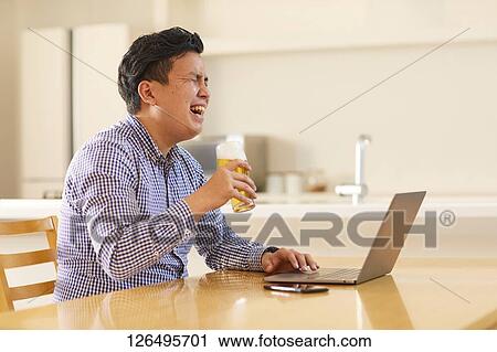 Stock Image - Japanese man drinking at home remote drinking. Fotosearch