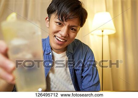 Stock Image - Japanese man drinking at home remote drinking. Fotosearch