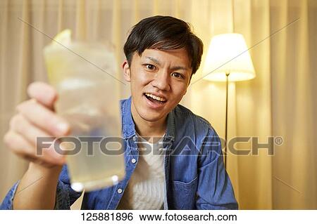 Stock Photograph - Japanese man drinking at home remote drinking. Fotosearch
