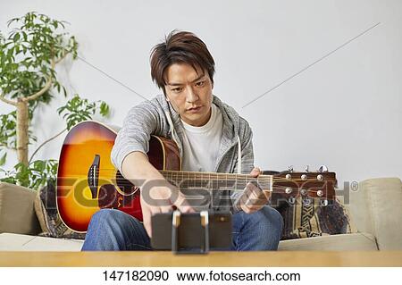 Stock Image - Japanese man playing guitar at home. Fotosearch