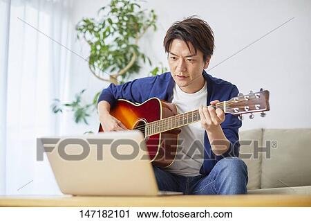 Stock Image - Japanese man playing guitar at home. Fotosearch