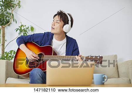 Stock Image - Japanese man playing guitar at home. Fotosearch