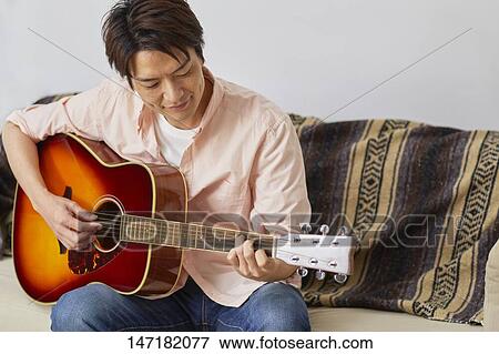 Stock Photo - Japanese man playing guitar at home. Fotosearch